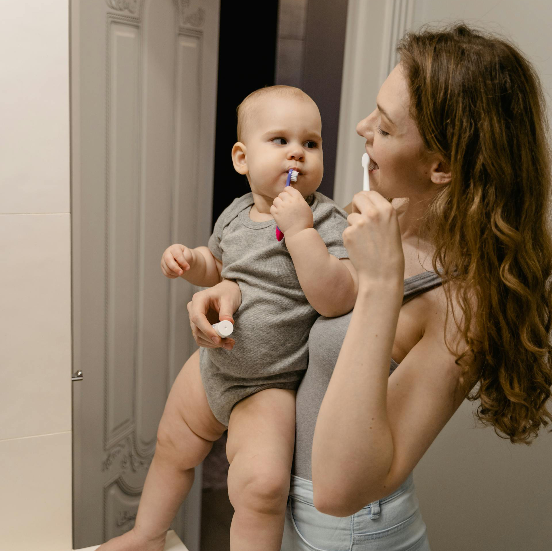 Modern residential bathroom interior with neutral colors; mother and child brushing teeth together.
