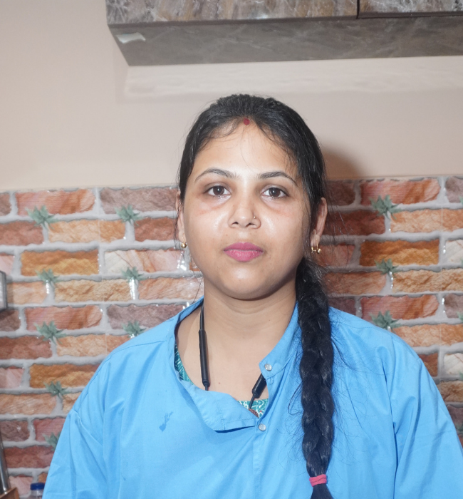 Female dental professional in a blue scrub top posing confidently against a brick-patterned clinic wall.