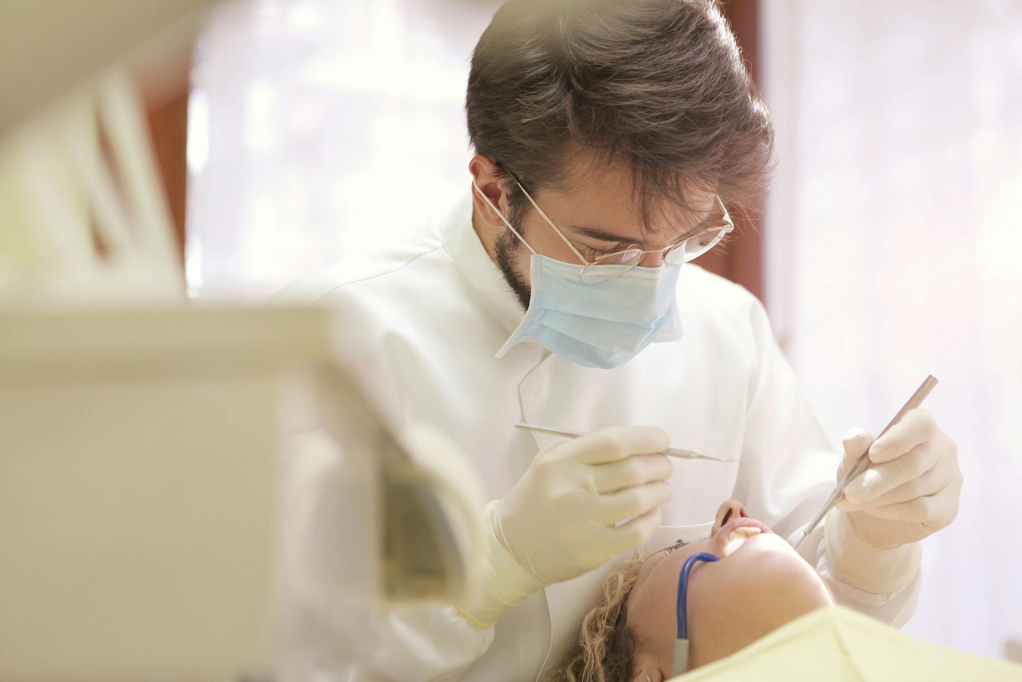 Dentist wearing mask and gloves examining patient’s teeth during routine dental checkup.