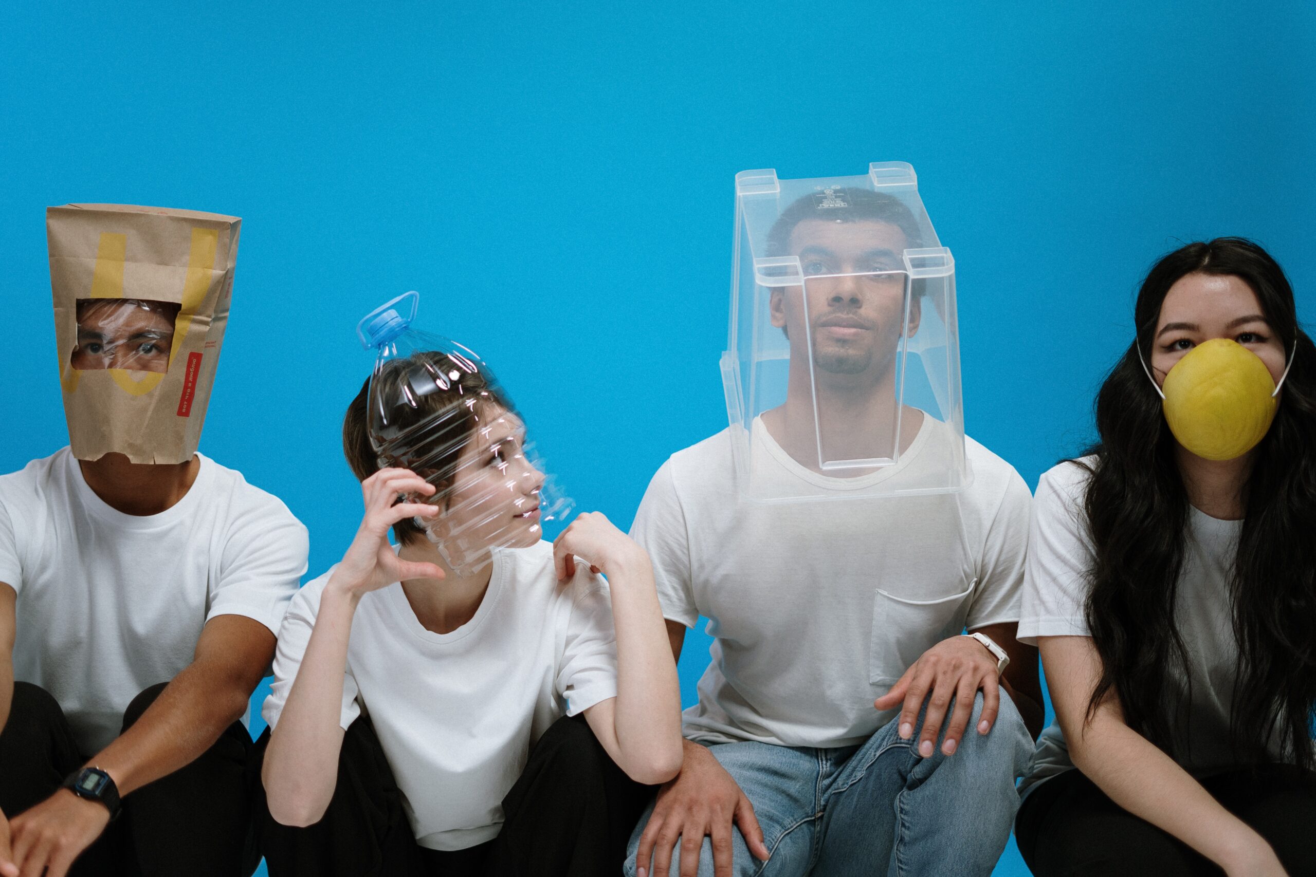Group of people wearing improvised face coverings made from household items against a bright blue background.