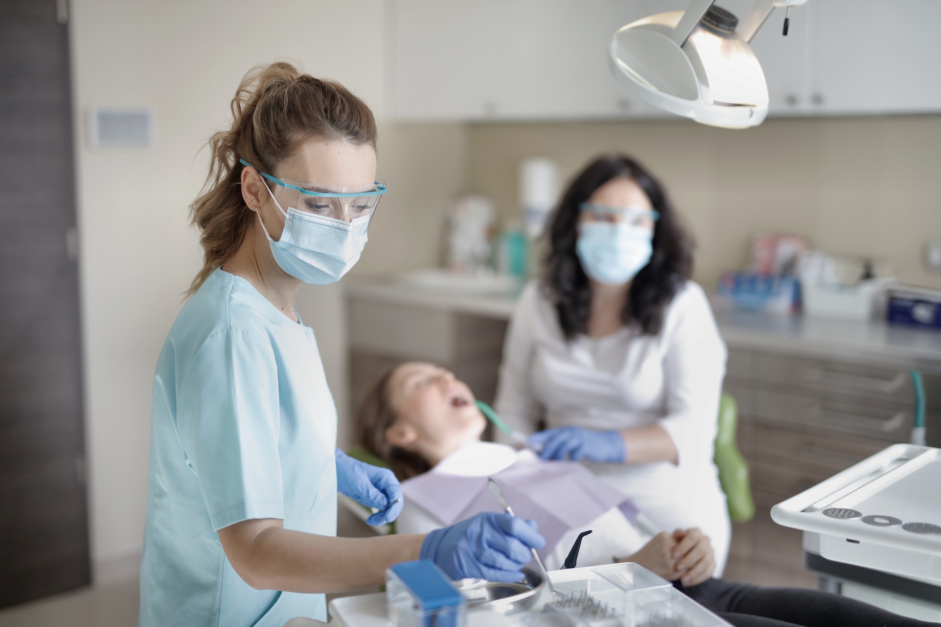 Dental assistant preparing instruments while a dentist treats a patient in a clean, modern clinical environment.