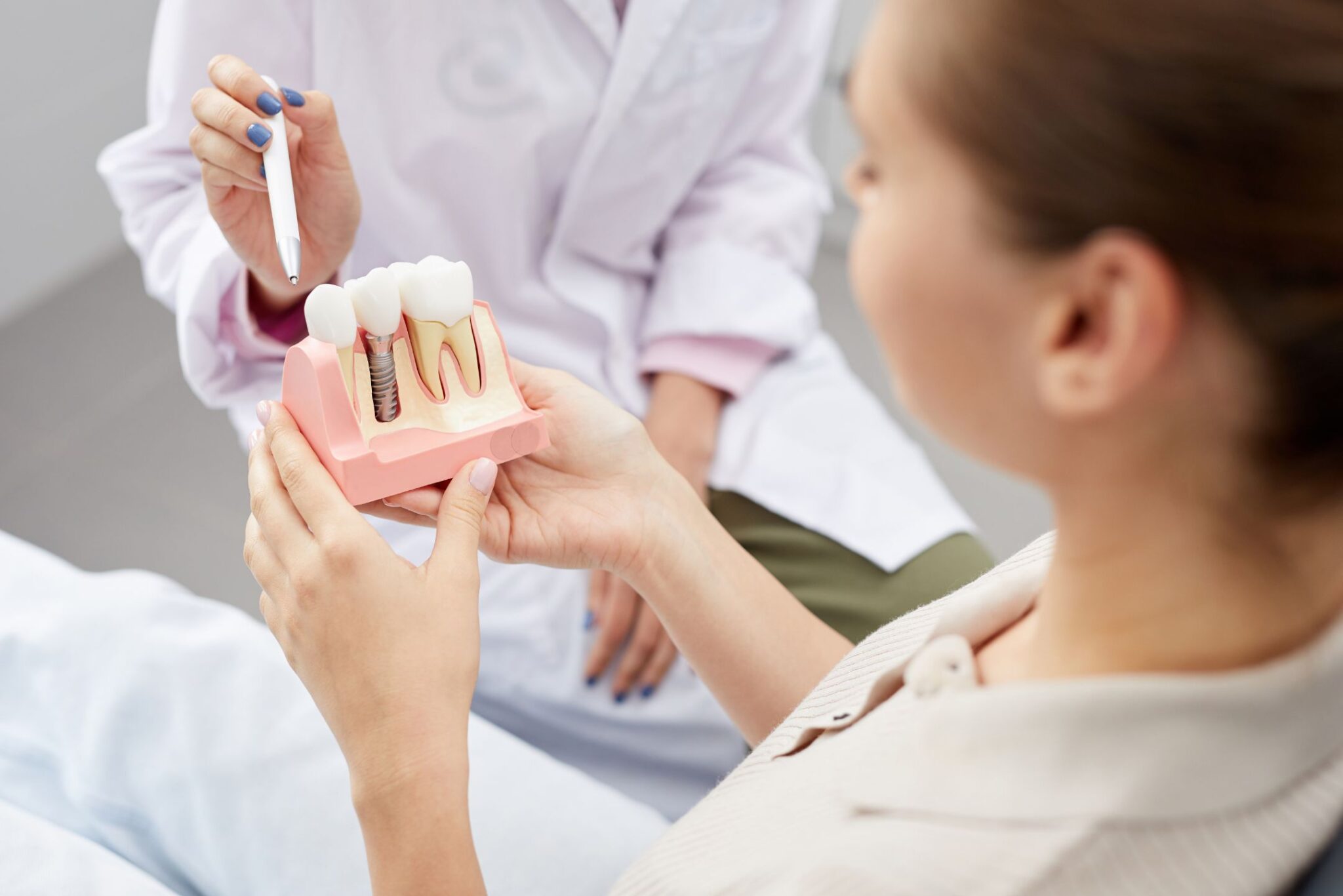 Dentist explaining dental implant procedure to a patient using an anatomical tooth model.