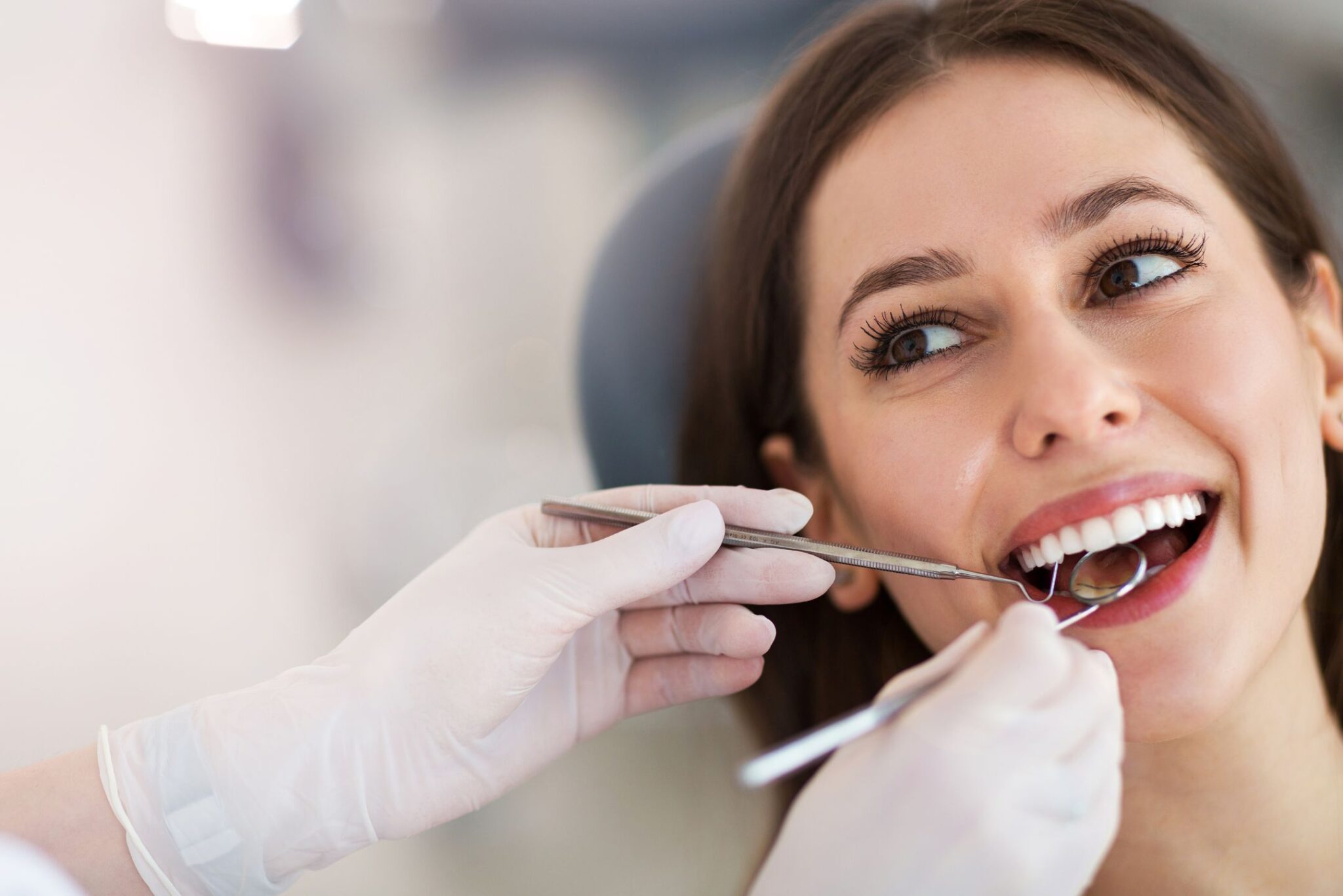 Dentist examining female patient’s teeth using dental mirror during routine oral checkup in a bright clinic.