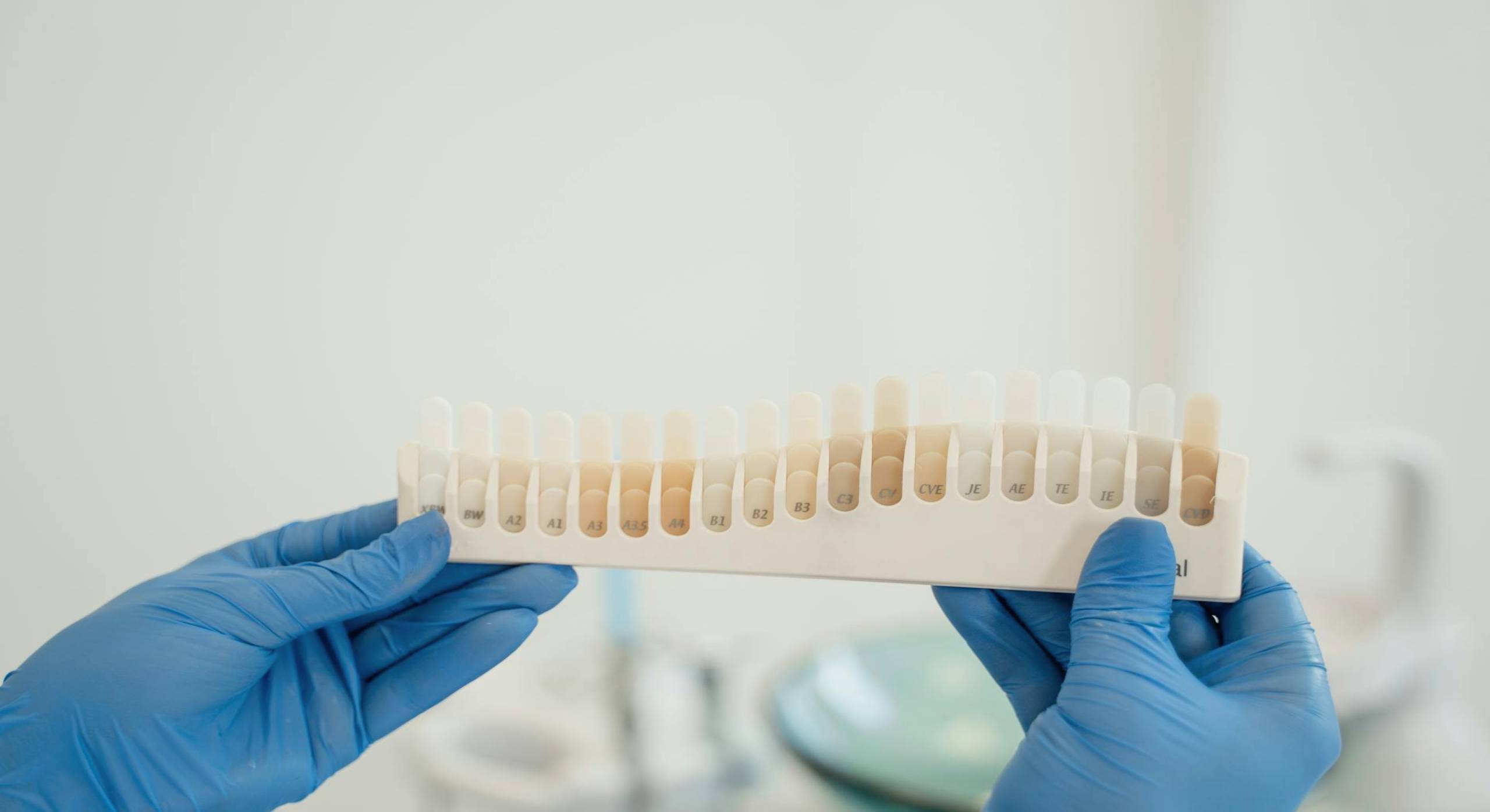 Gloved hands holding a dental shade guide used to match tooth color for whitening or restorations.